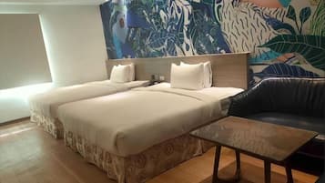 A hotel room with two beds, a sofa, a coffee table, and a large tropical-themed wall mural.