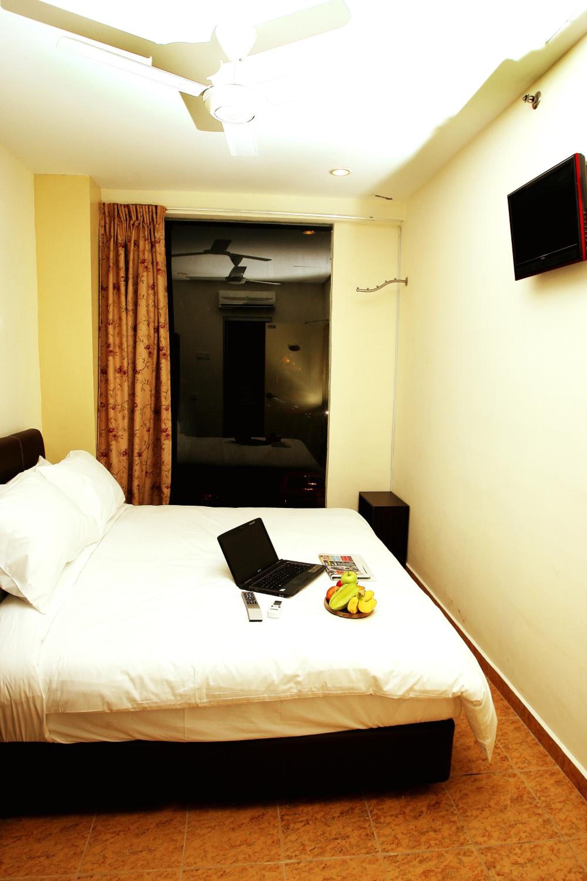 A hotel room with a bed, a laptop, a remote control, and a fruit bowl on the bed.