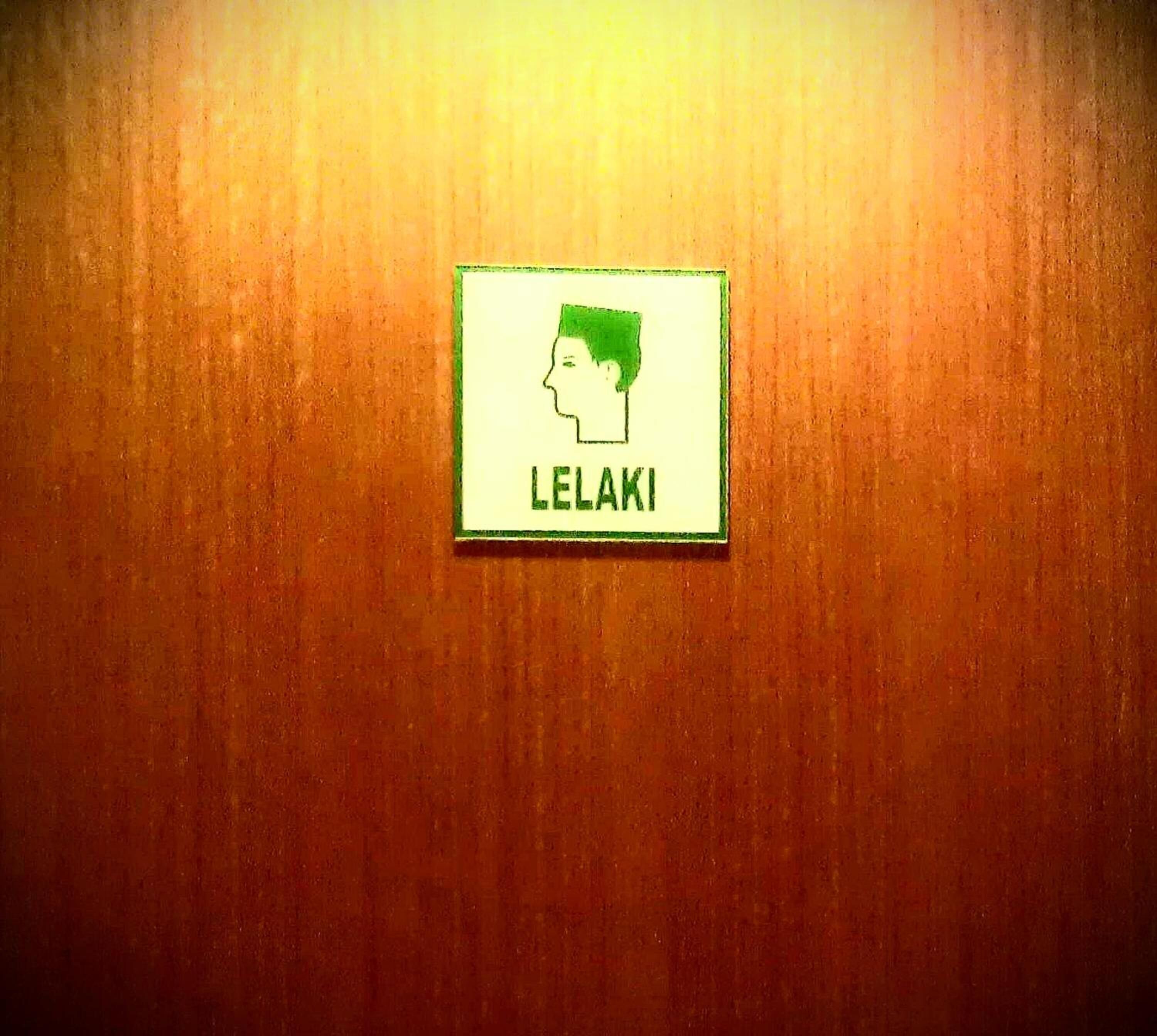A wooden wall with a sign that reads "LELAKI" and a green outline of a head.