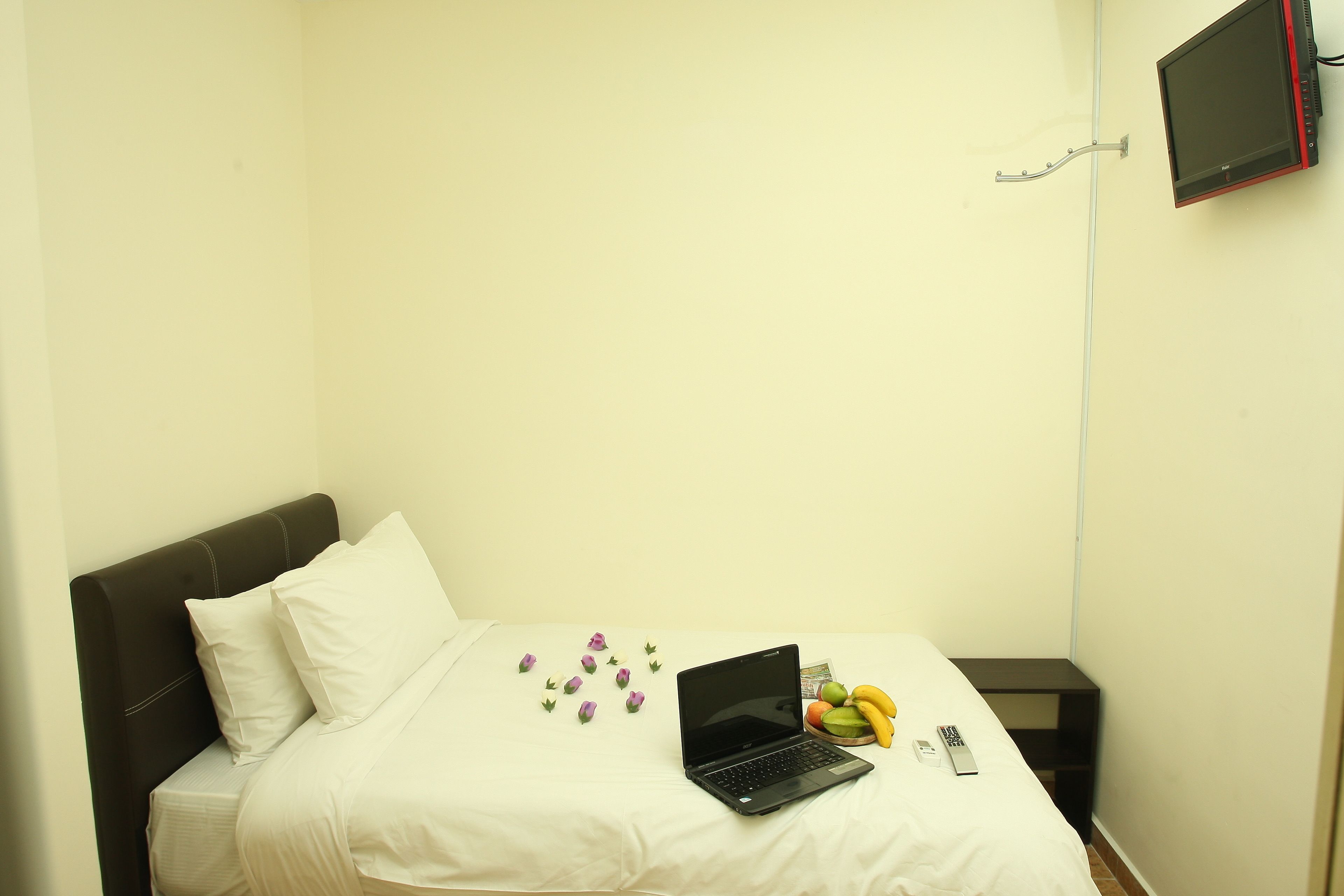 A small, neatly made bed with a laptop, bananas, and a remote control on it.