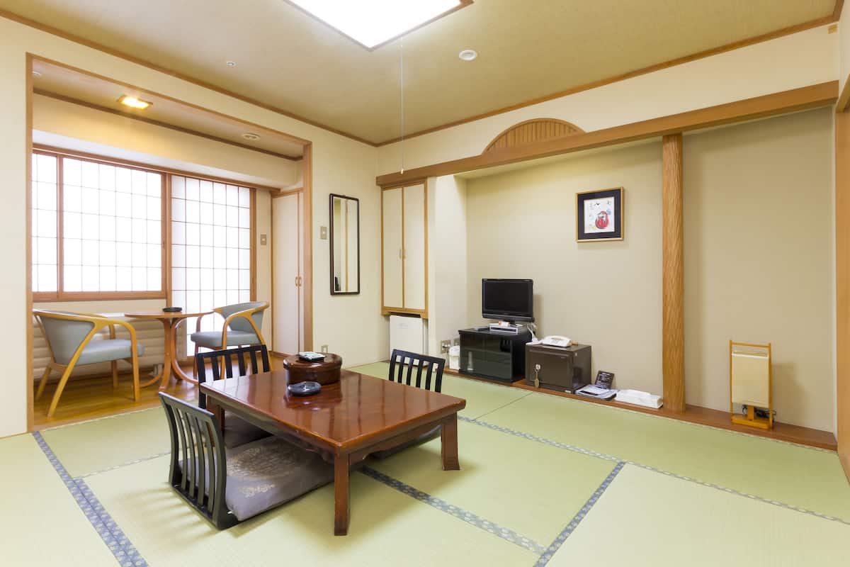 A traditional Japanese room with tatami flooring, a wooden dining table, chairs, a television, and a small cabinet.