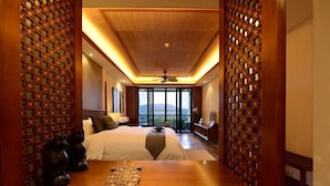 A hotel room with a large bed, wooden headboard, a wooden table with a decorative item, and a view of the outdoors. - Shixishu Jianguo Yalong Bay Resort Hotel (Sanya)