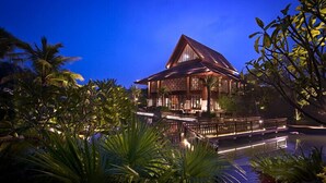 A wooden building with a balcony, surrounded by lush greenery and a body of water. - Shixishu Jianguo Yalong Bay Resort Hotel (Sanya)