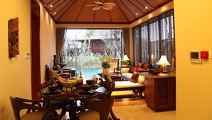 A dining area with a round table, chairs, and a view of a garden through large windows. - Shixishu Jianguo Yalong Bay Resort Hotel (Sanya)