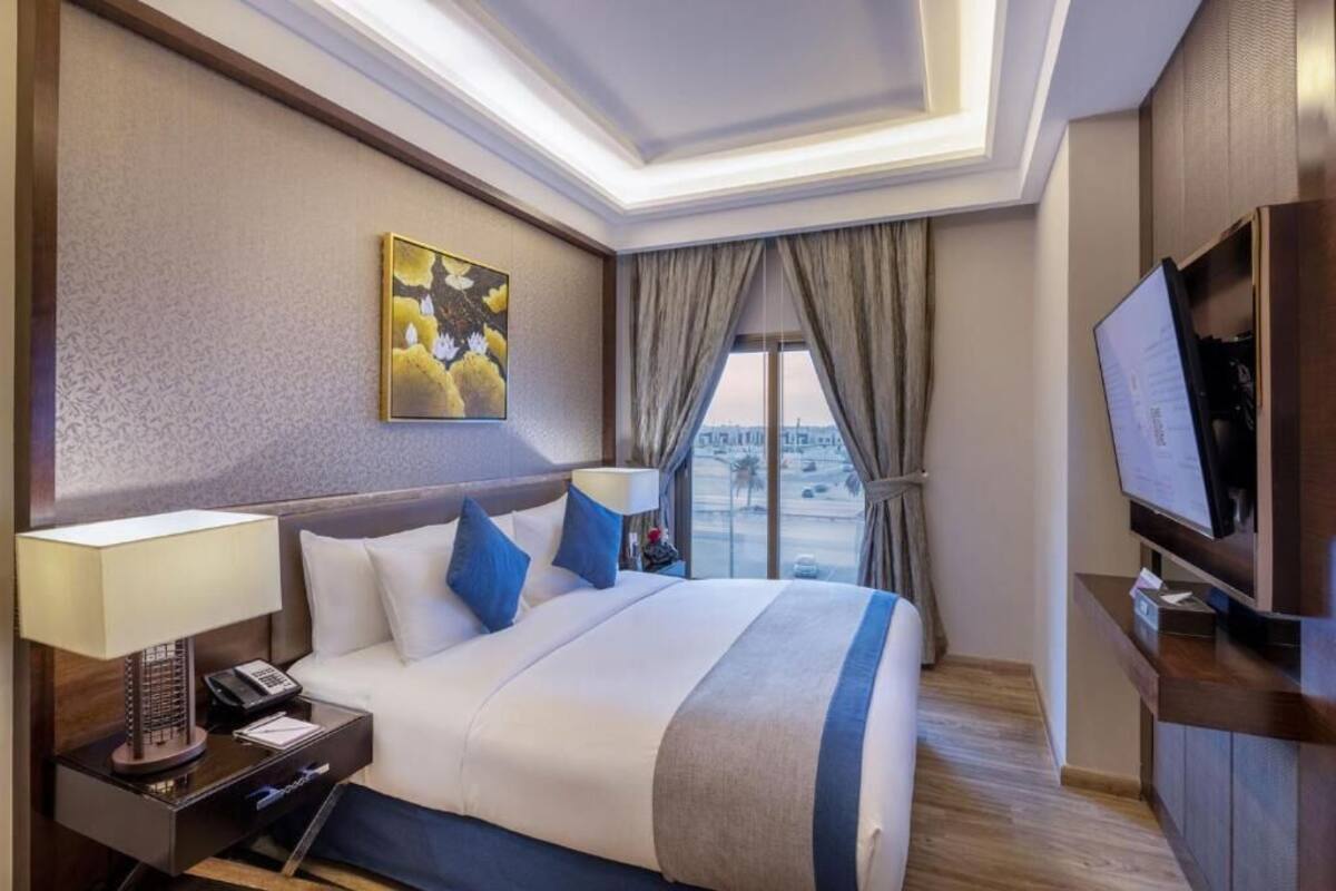 A hotel room with a bed, a TV, a desk with a lamp, a phone, and a window with curtains.