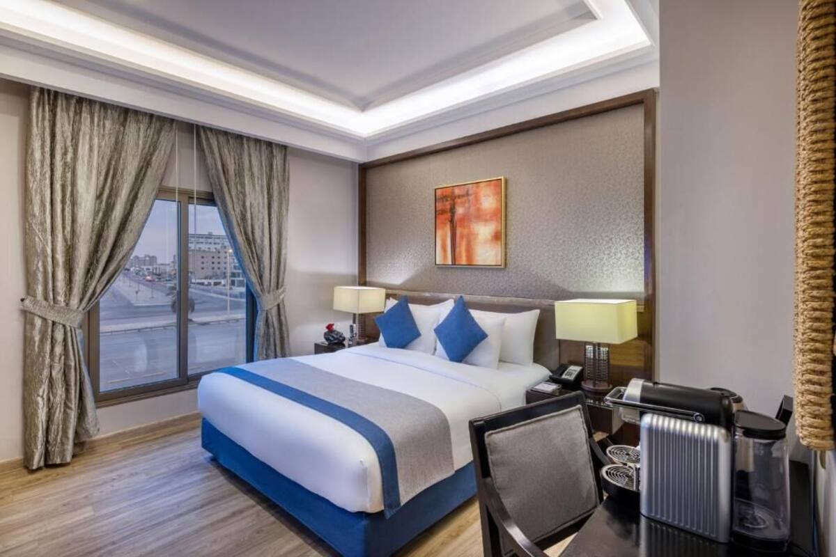 A hotel room with a large bed, two bedside tables with lamps, a coffee maker, and a view of the city through the window.