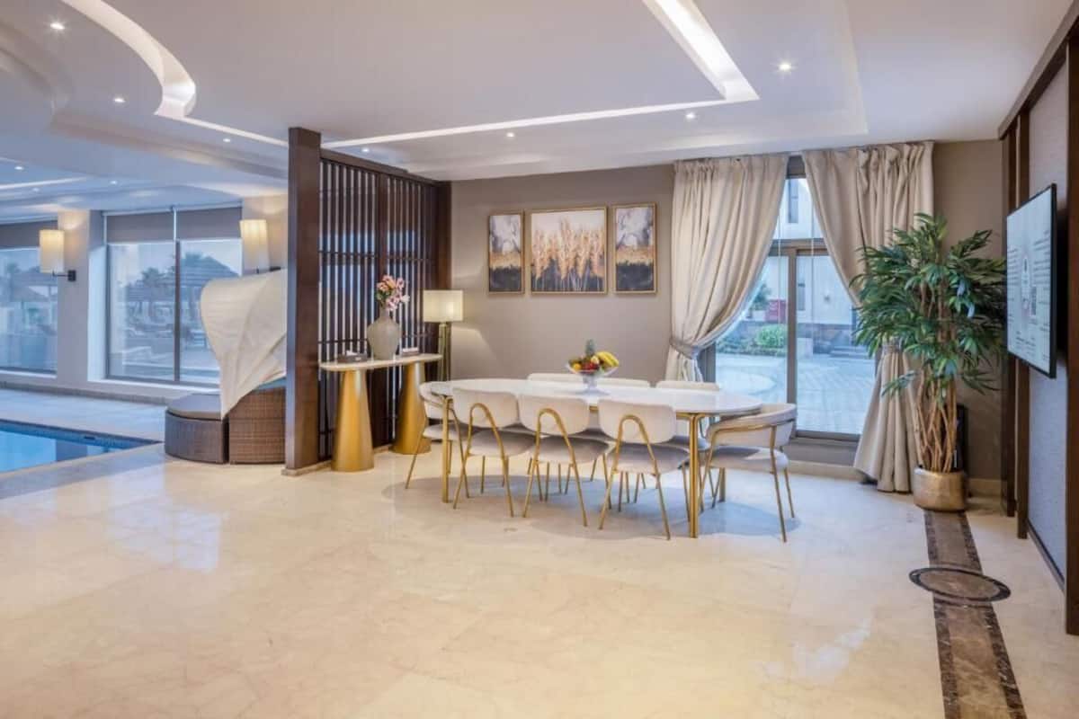 A modern dining area with a round table and chairs, a pool, and large windows.