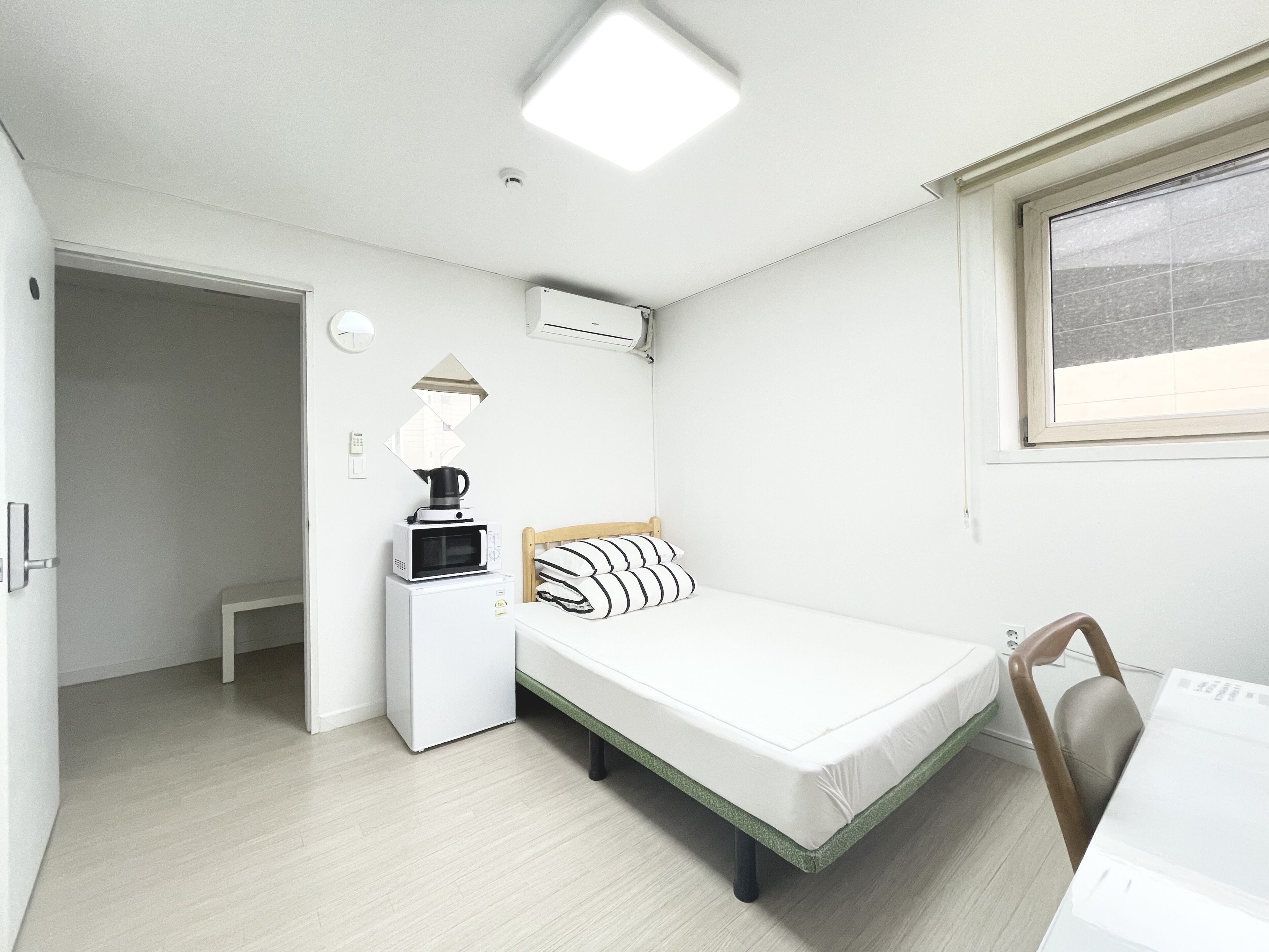 Une chambre d’hôtel de taille réduite, équipée d’un lit, d’un petit bureau, d’un four à micro-ondes et d’un appareil de climatisation.