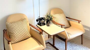 A room with two beige armchairs, a small table with a lamp, a telephone, and a plant.