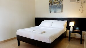 A neatly made bed with white linens and towels, a black headboard, a nightstand with a lamp, and a painting of palm trees on the wall. - La Playa Estrella Beach Resort (Santa Fe)