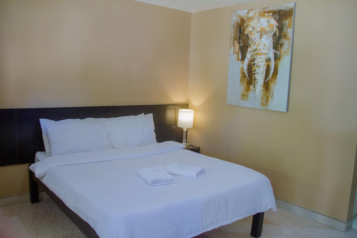 Quarto de hotel com cama bem arrumada, mesa de cabeceira com abajur e uma grande pintura abstrata na parede.