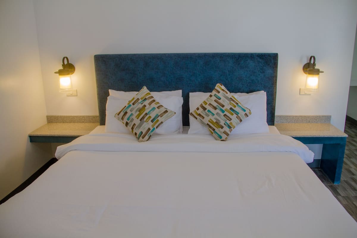 Quarto de hotel com uma cama grande, duas almofadas com padrão geométrico e duas luminárias de cabeceira.