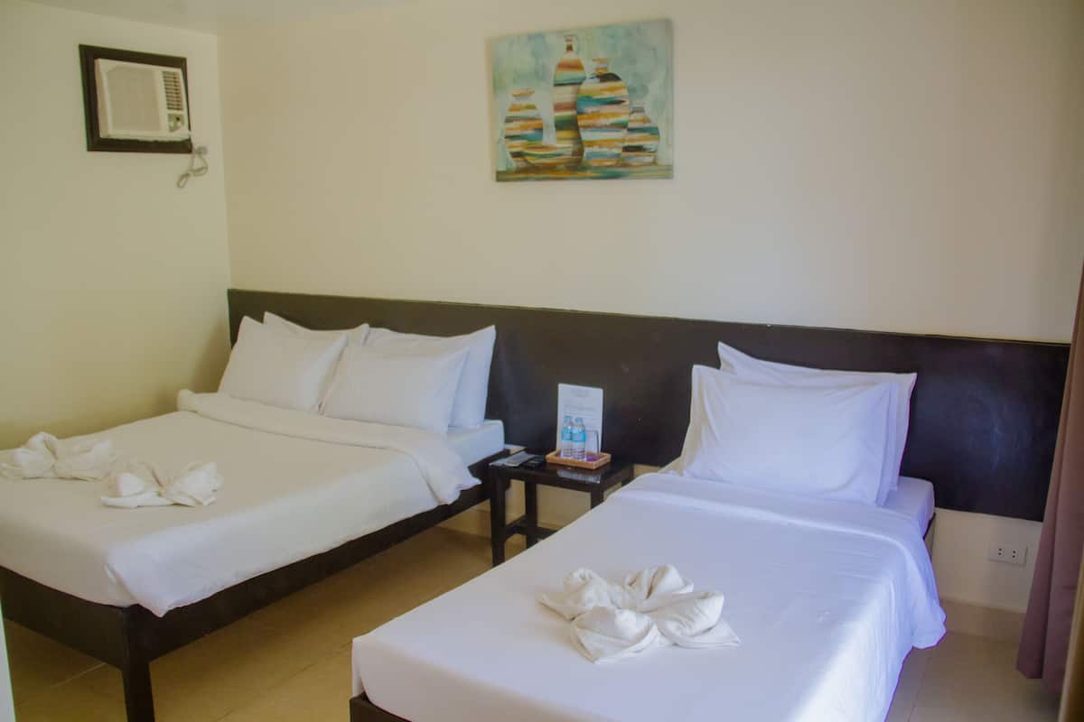 Duas camas bem arrumadas com roupa de cama e toalhas brancas, uma pequena mesa com uma garrafa de água e um quadro na parede.