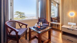 A hotel room with a large window, two wooden chairs, a glass table with a coffee pot, and a bedside phone. - Treebo Varuna with Mountain View, Mall Road (Shimla)