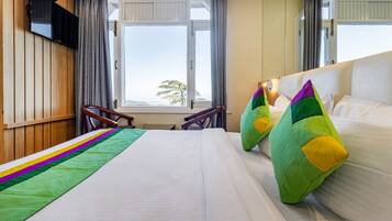 Habitación de hotel con una cama grande, un televisor montado en la pared, una ventana con cortinas y vistas al exterior.