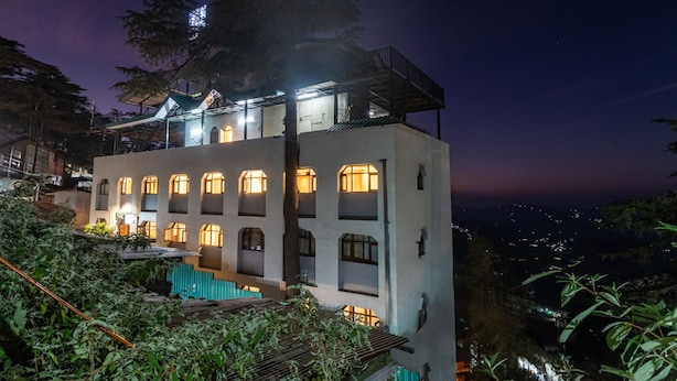 A multi-story building with multiple windows and a balcony, surrounded by greenery. - Treebo Varuna with Mountain View, Mall Road (Shimla)