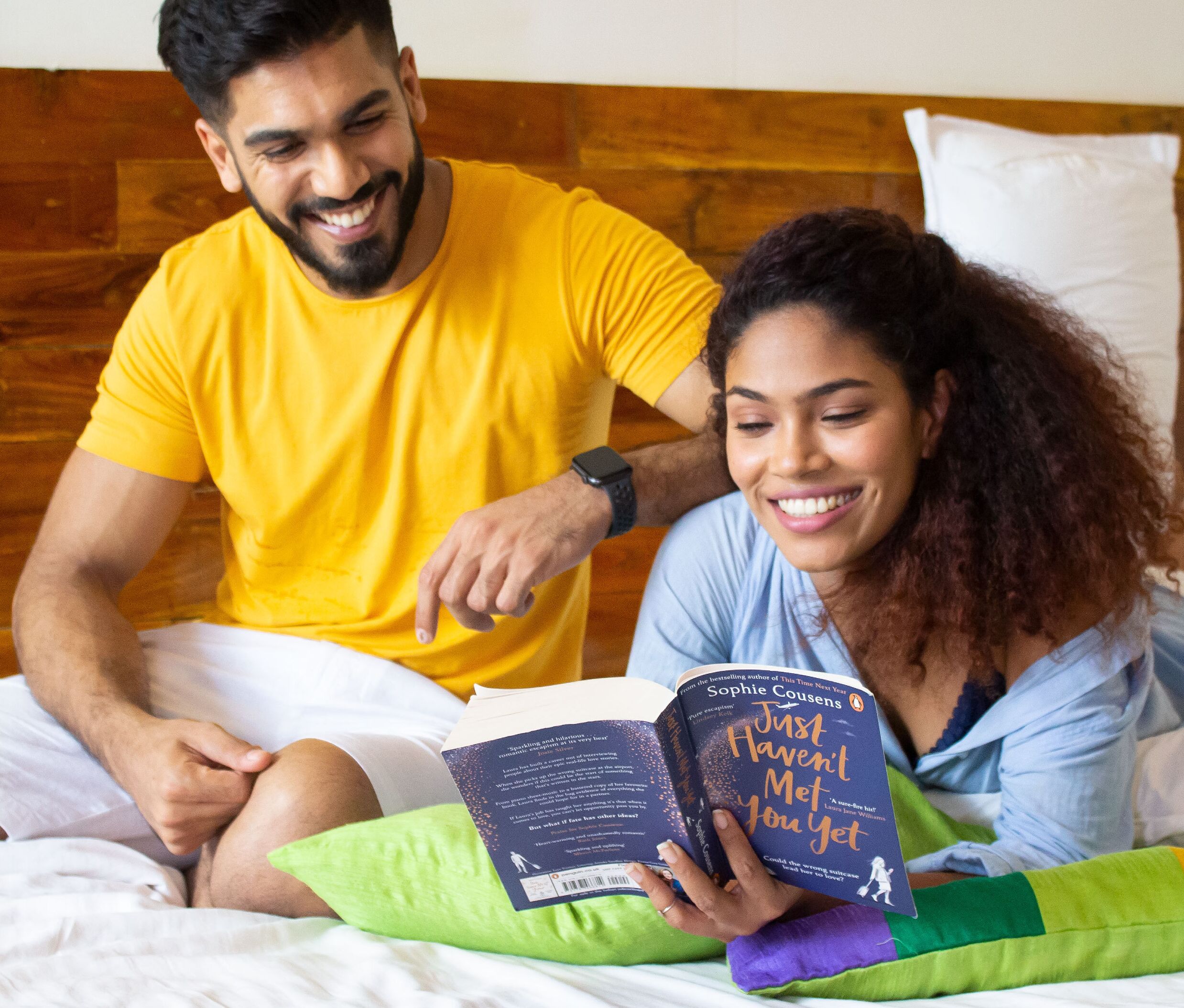 A person reading a book on a bed with a wooden headboard.