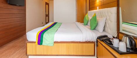 A hotel room with a wooden bed, a flat-screen TV mounted on the wall, a bedside table with a phone, and a mirror.