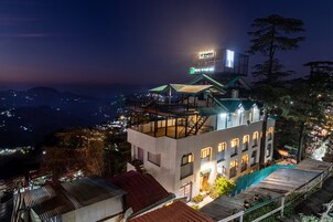 Un edificio de varios pisos con terraza en la azotea, un cartel y vistas del entorno.