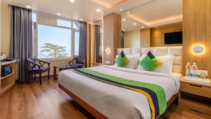 A hotel room with a large bed, a desk, a chair, a TV, and a window with curtains. - Treebo Varuna with Mountain View, Mall Road (Shimla)