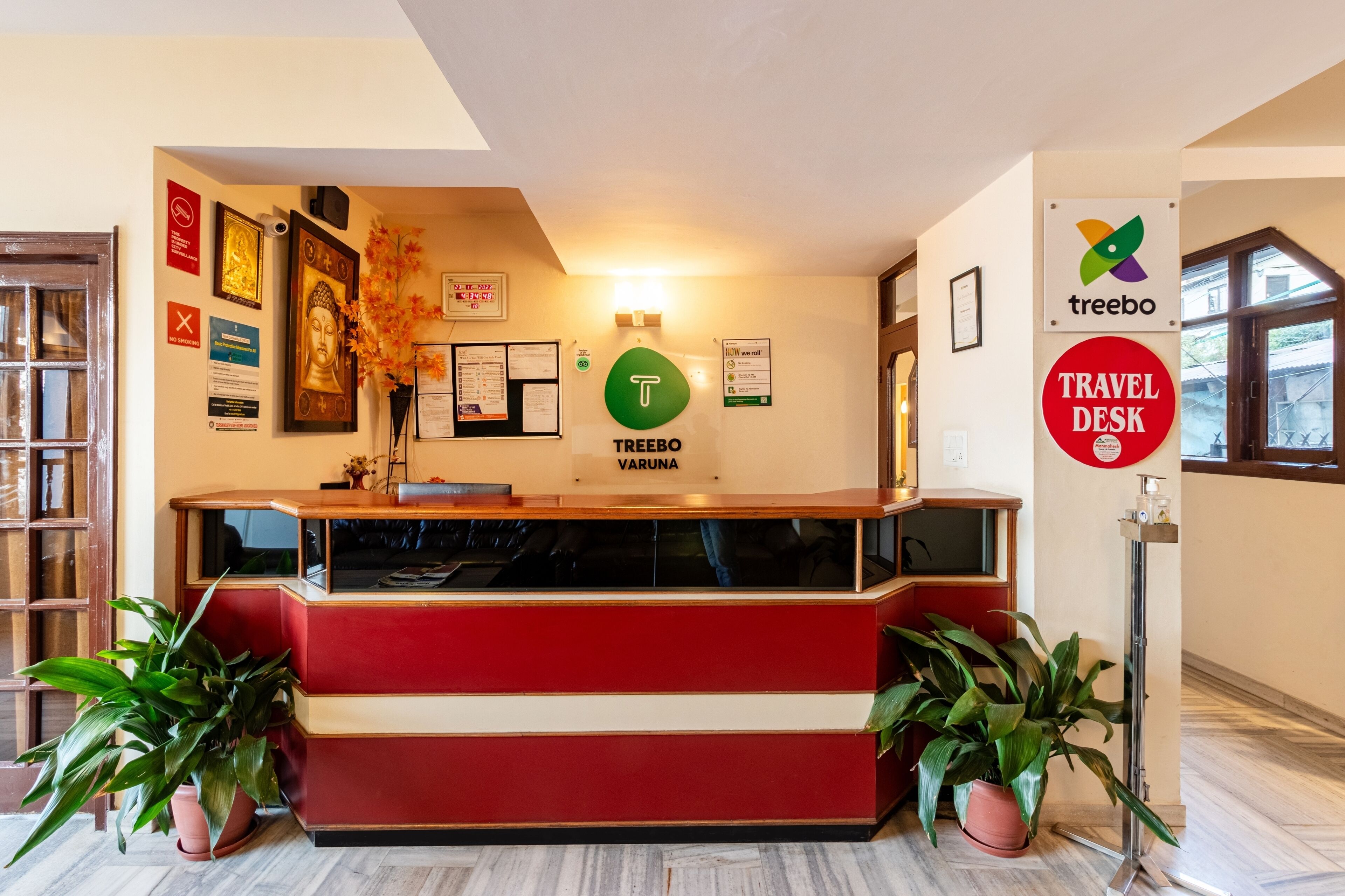 A reception desk with a red and white color scheme, a 'Treebo' sign, a 'Travel Desk' sign, and a 'T' logo.