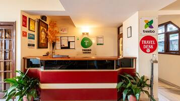 A reception desk with a red and white color scheme, a 'Treebo' sign, a 'Travel Desk' sign, and a 'T' logo.