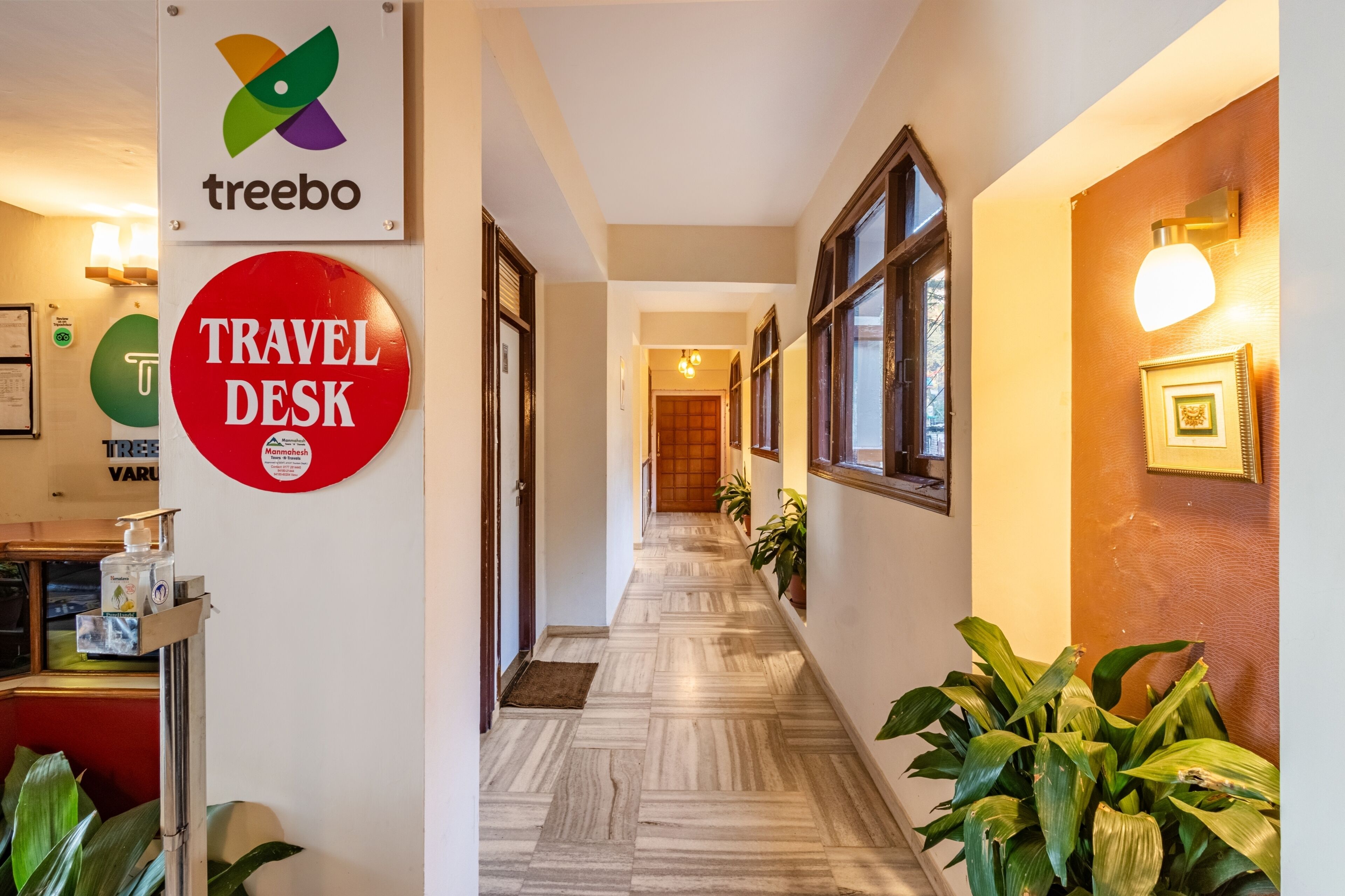 A hotel corridor with a travel desk, a treebo sign, and a wooden floor.