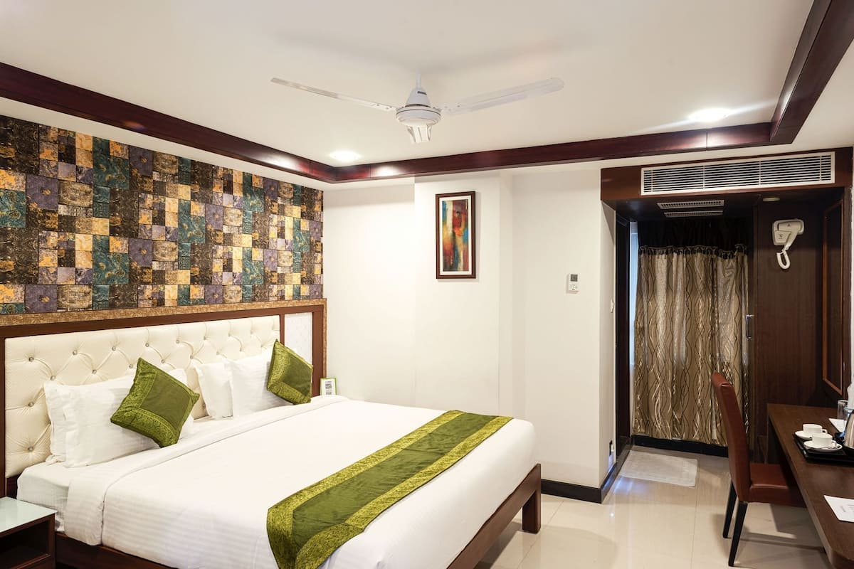 Habitación de hotel con una cama grande, ventilador de techo, un cuadro, teléfono y puerta que da a un baño.