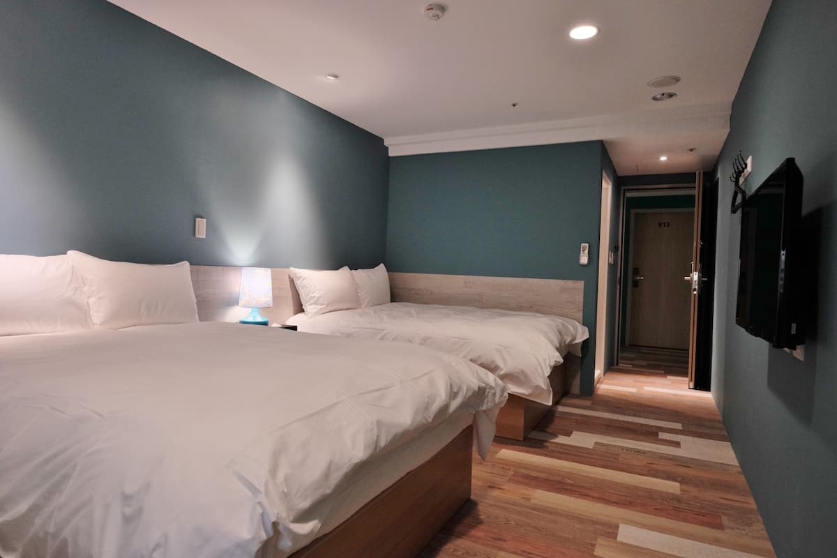 A modern hotel room with two beds, a wooden floor, and a blue accent wall.