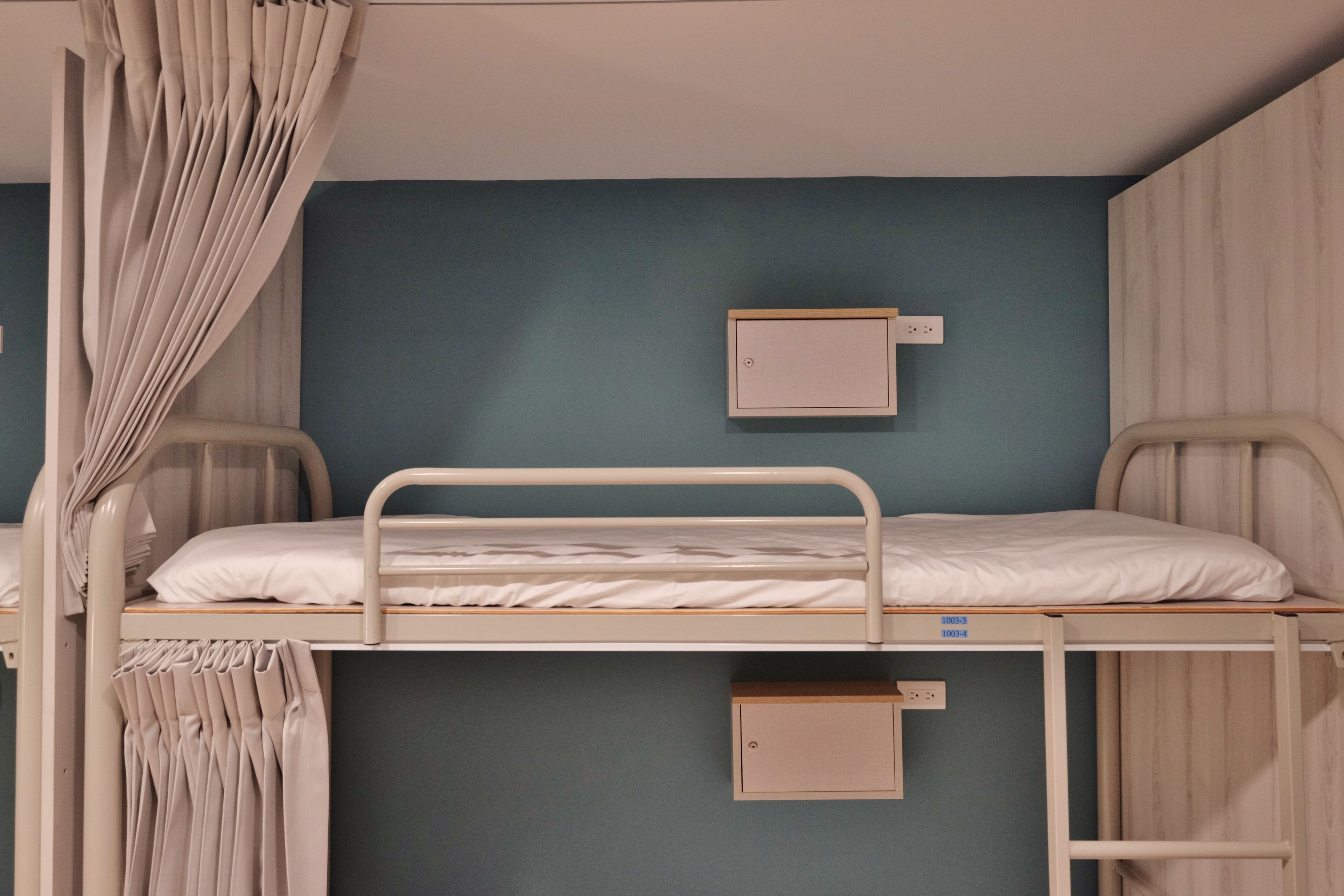 A bunk bed room with a curtain, a small cabinet, and a wall-mounted electrical outlet.