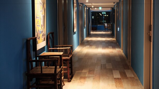 Un couloir avec des chaises et des tables en bois, des murs bleus et des tableaux encadrés accrochés aux murs.