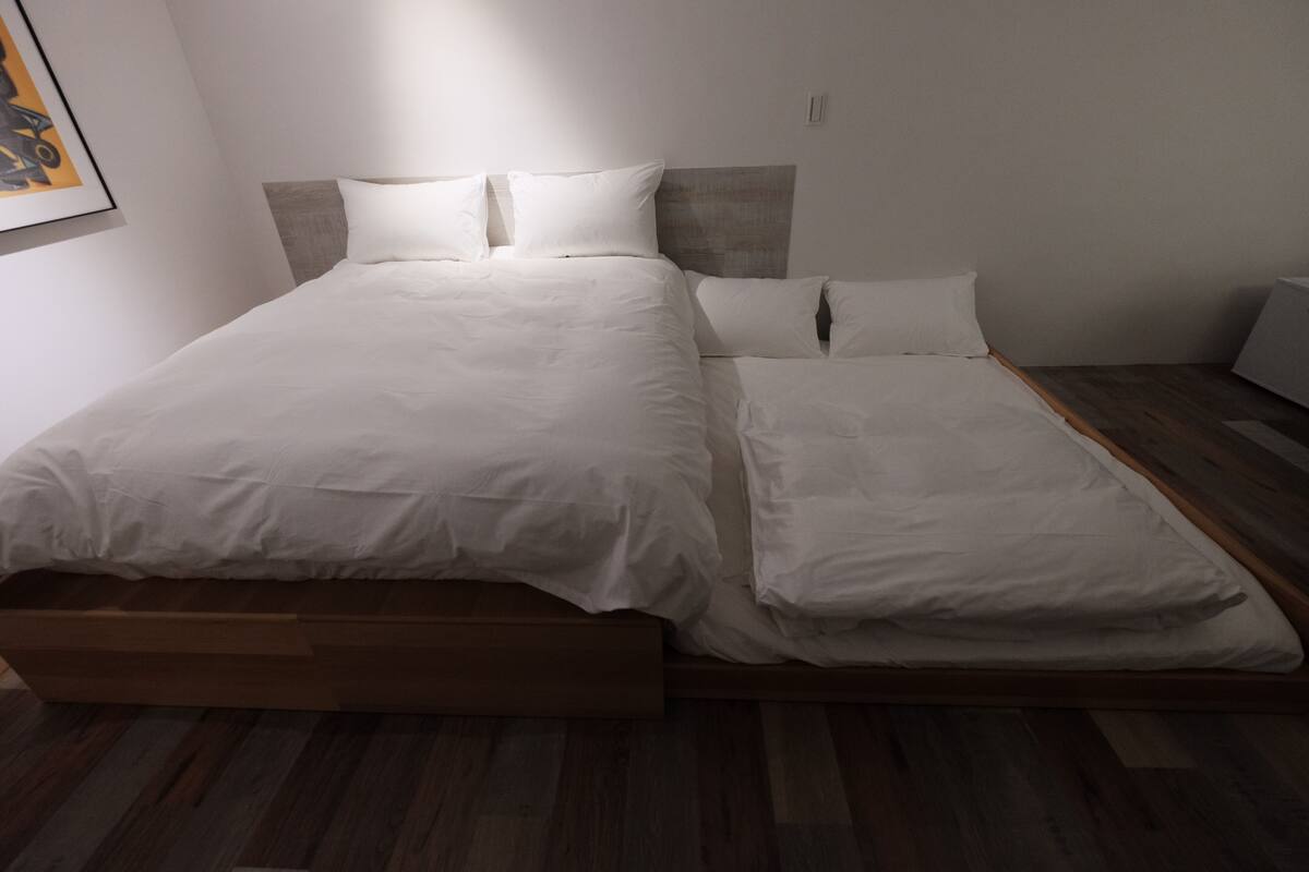 A modern bedroom with a wooden bed frame, white bedding, and a minimalist design.