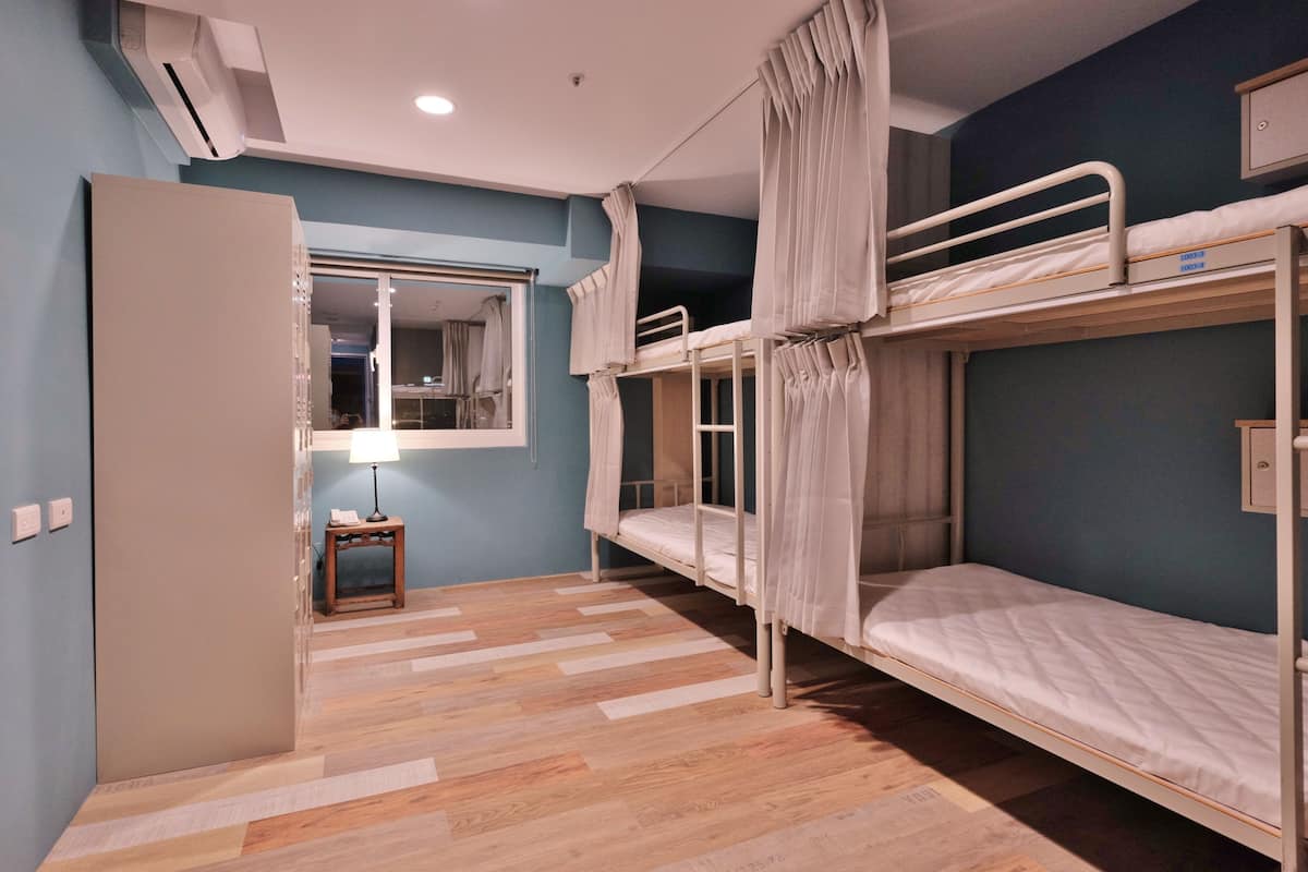 A room with bunk beds, a small table with a lamp, and a mirror on the wall.