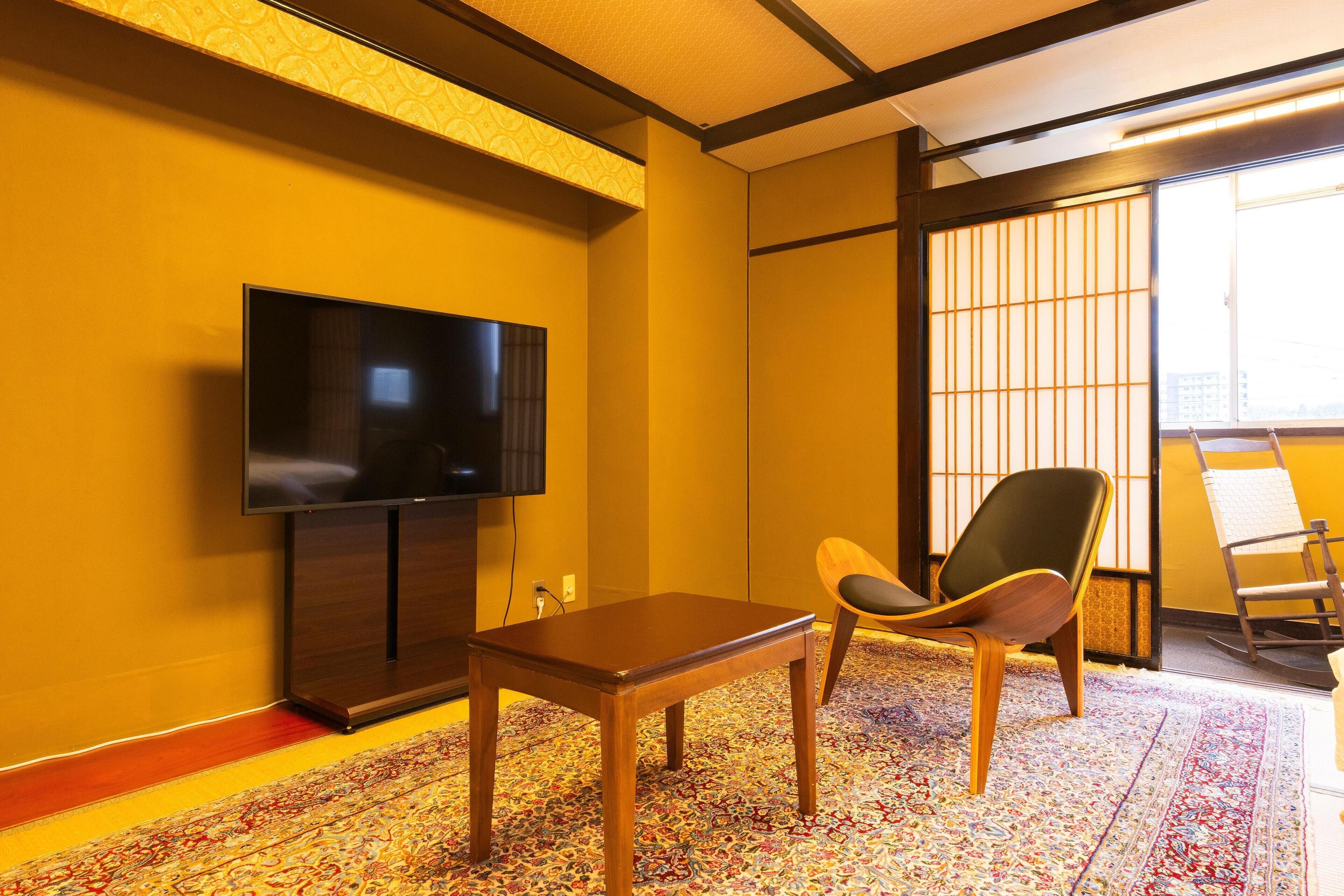 A room with a television on the wall, a wooden table, and a chair.