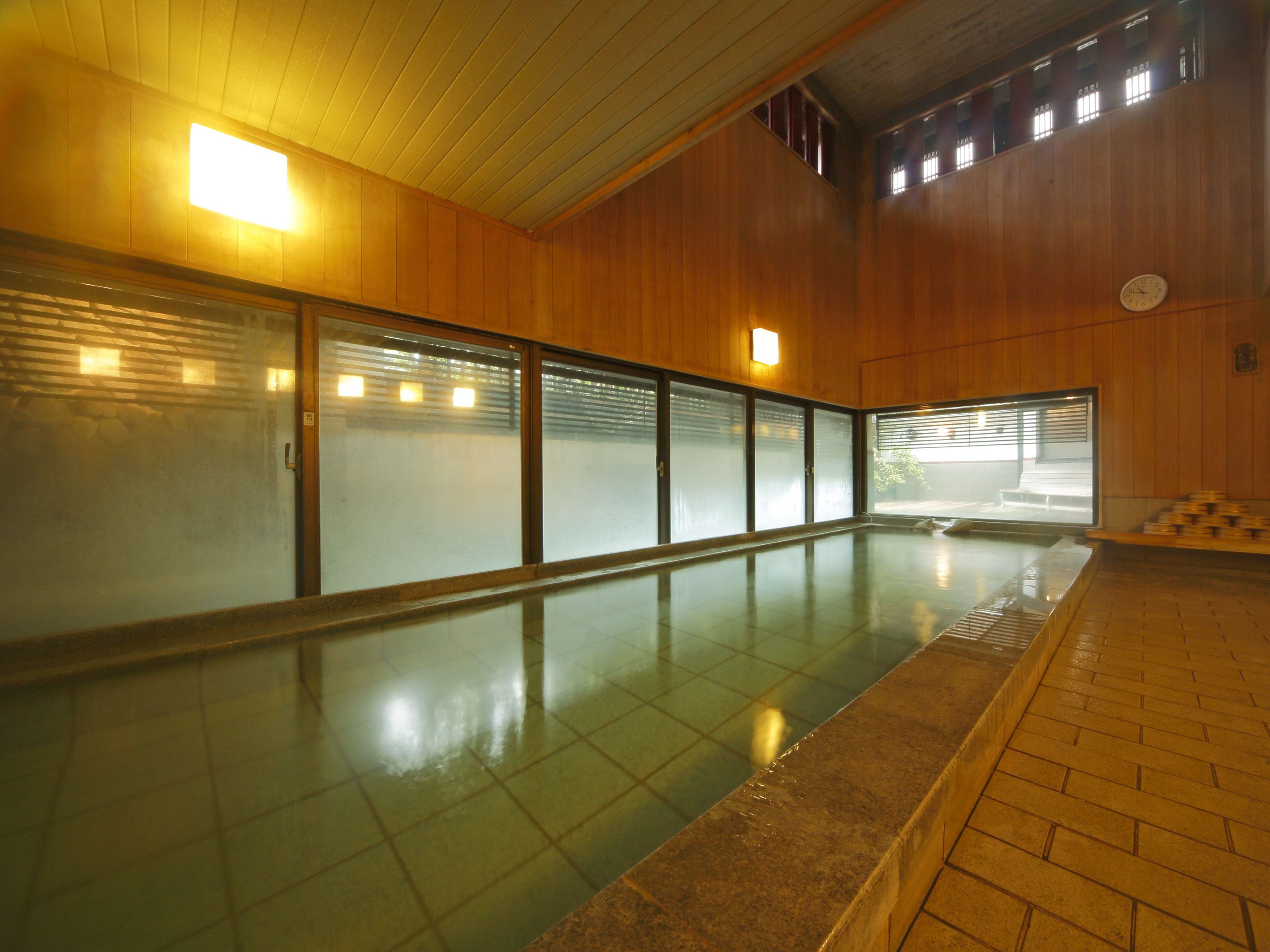 Una amplia piscina interior con suelo de baldosas, paredes de madera y puertas de vidrio esmerilado.