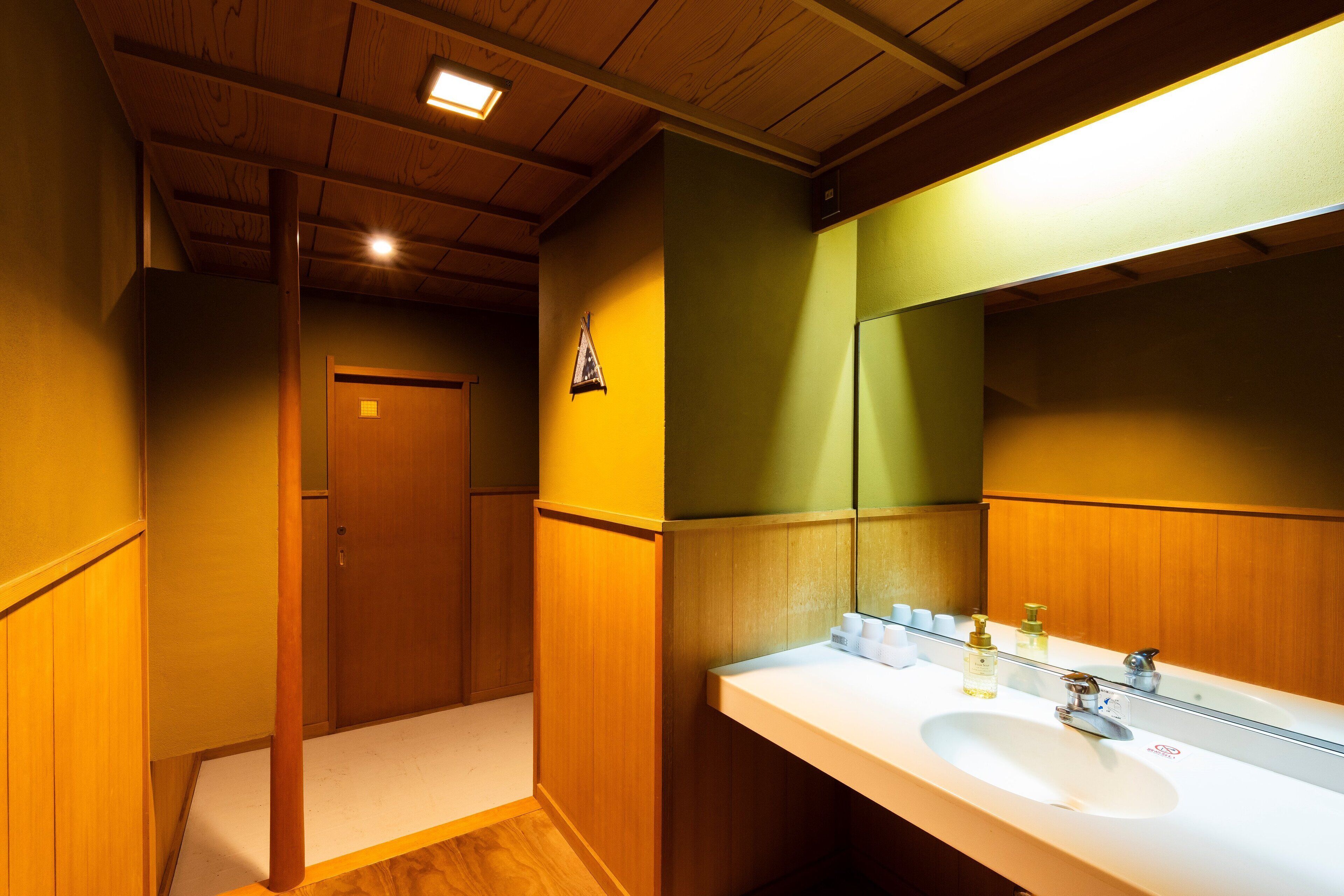Un baño con paneles de madera, un lavamanos blanco y un espejo que refleja la habitación.