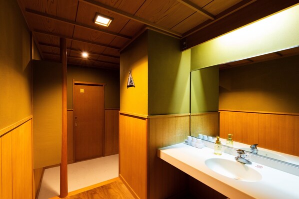 A bathroom with wooden paneling, a white sink, and a mirror reflecting the room. - Kyotoya (Takeo)