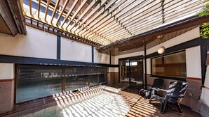 A sunlit outdoor area with a wooden pergola, a glass enclosure, and two Adirondack chairs.
