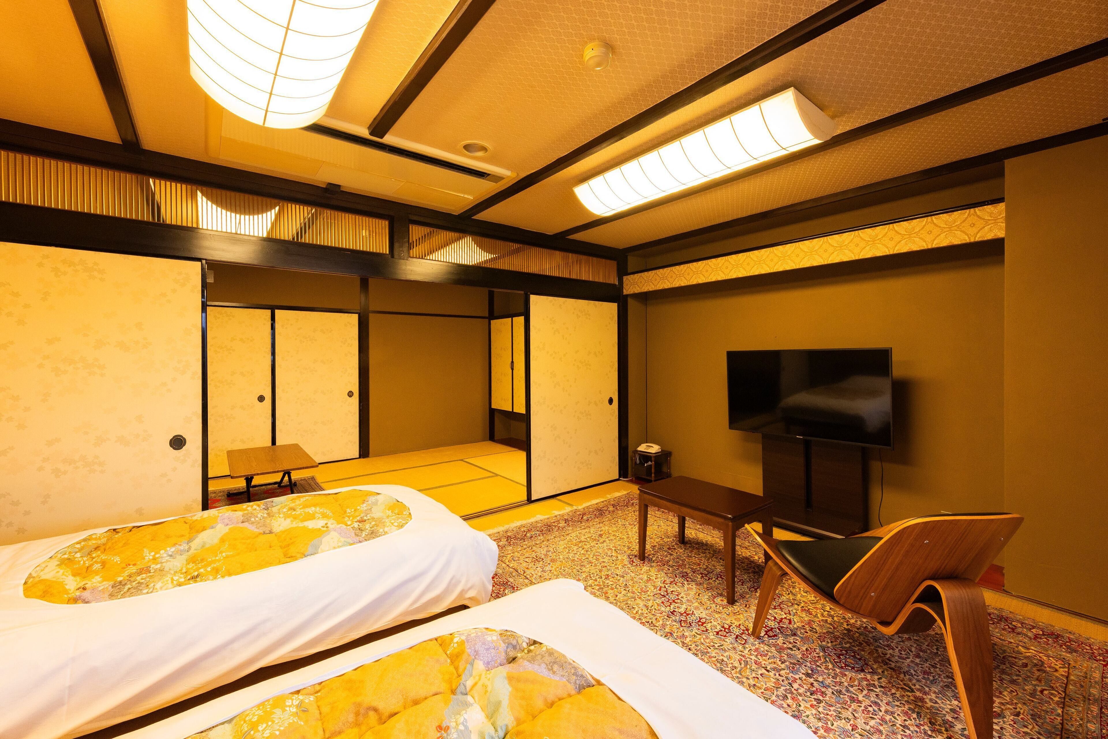 Ein Hotelzimmer mit zwei Betten, einem Fernseher, einem kleinen Tisch und einem Stuhl.