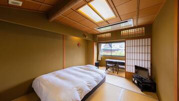 Una habitación tradicional japonesa con suelo de tatami, una cama, un televisor sobre un soporte y una puerta corredera con vistas al exterior.