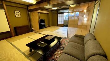 Una habitación tradicional japonesa con tatamis, un sofá, una mesita y un televisor.