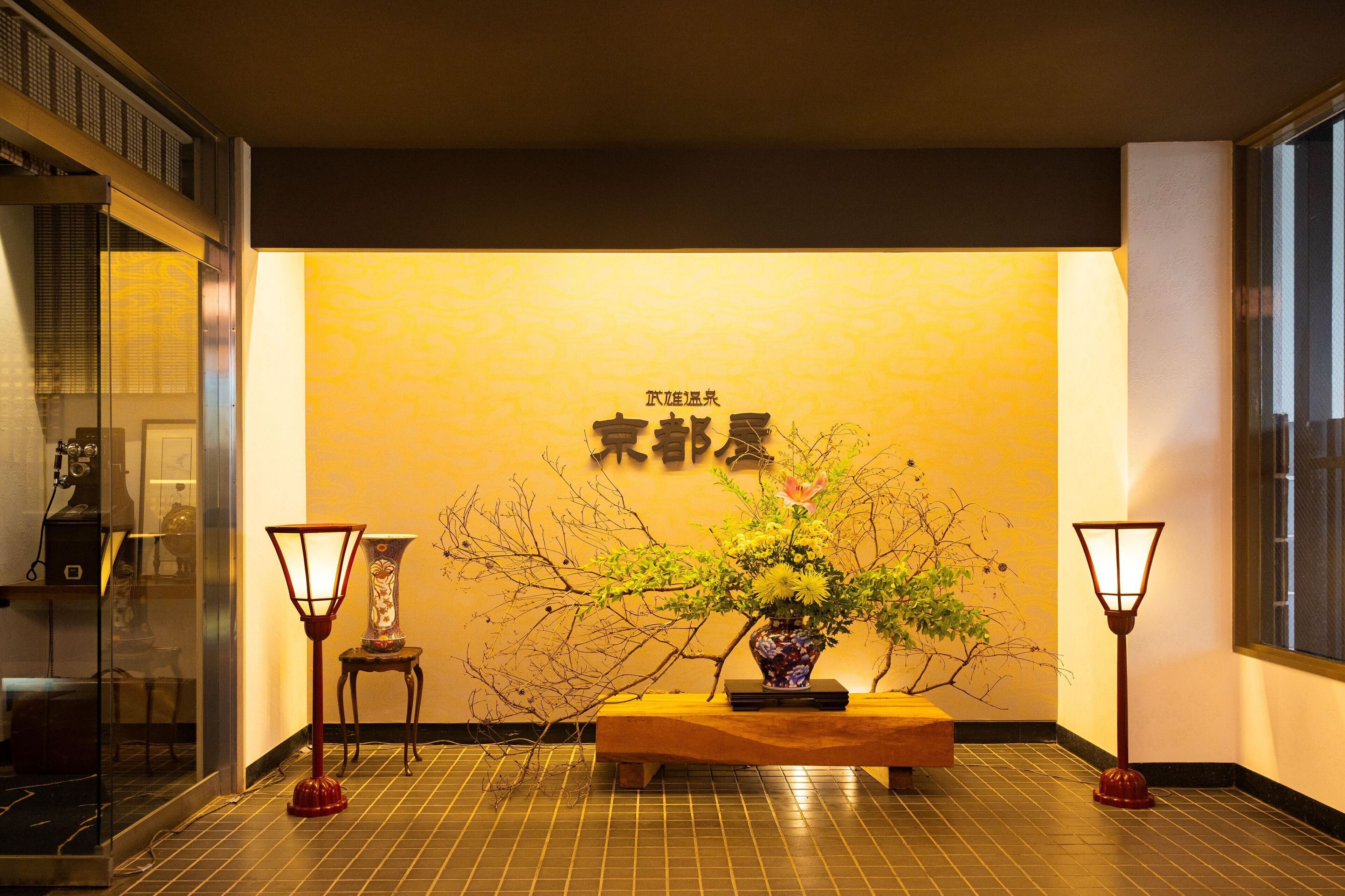 A reception area with a wooden bench, two floor lamps, a vase with flowers, and a wall with Chinese characters.