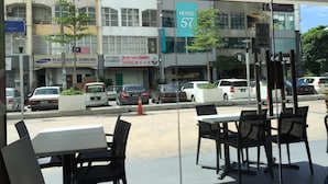 An outdoor seating area with tables and chairs, a view of a hotel with a sign reading "HOTEL 57", and several parked cars. - Hotel 57 Subang Jaya (Subang Jaya)