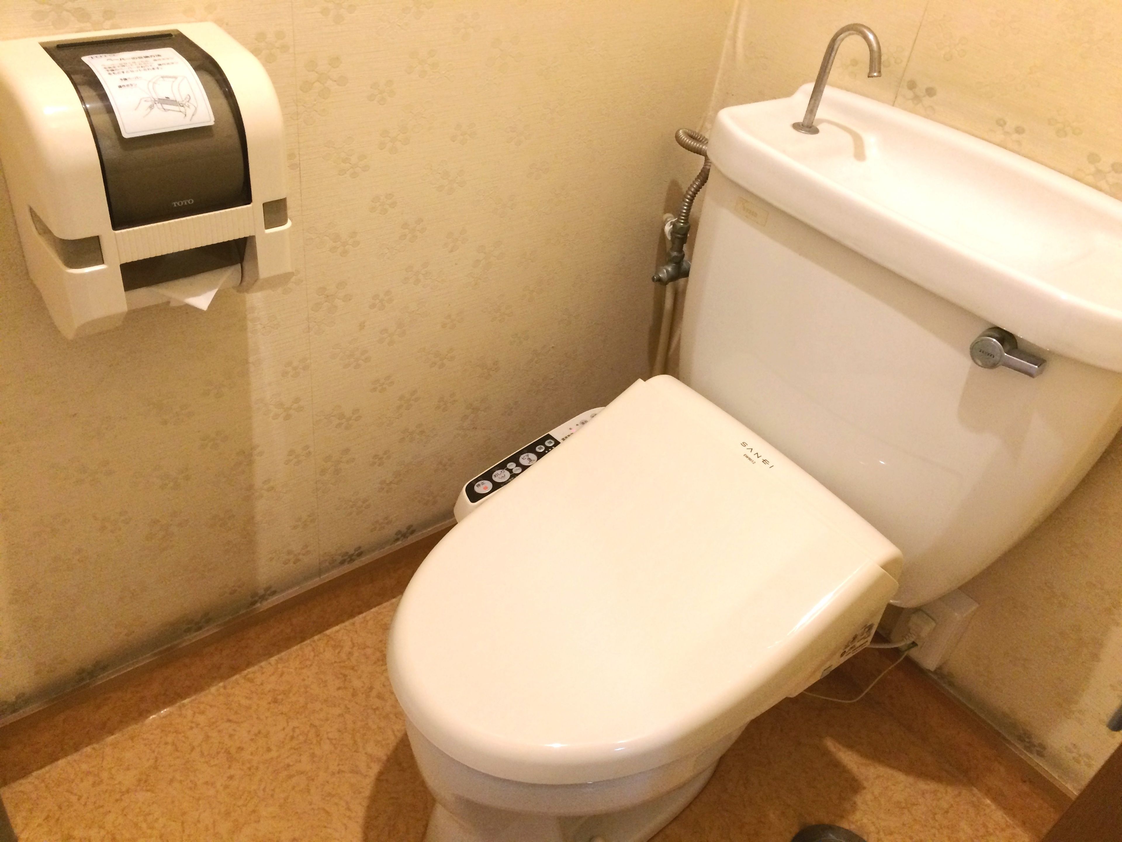 A toilet with a control panel, a paper towel dispenser, and a bidet attachment.