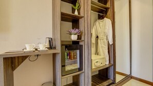 Hotelkamer met een houten wastafel, een spiegel, een badjas hangend aan een rek, en een plankje met een potplant en een koffiezetapparaat.