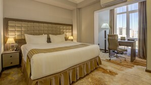 Een hotelkamer met een groot bed, een bureau, een stoel, een airconditioner en uitzicht op de stad door het raam.