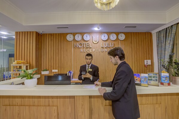 Mostrador de recepción de hotel con un panel de madera de fondo, un reloj y un letrero de recepción.