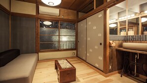 Una habitación japonesa tradicional con suelo de tatami, una mesa de madera baja, un sofá, una ventana con paneles shoji y una zona de lavabo.