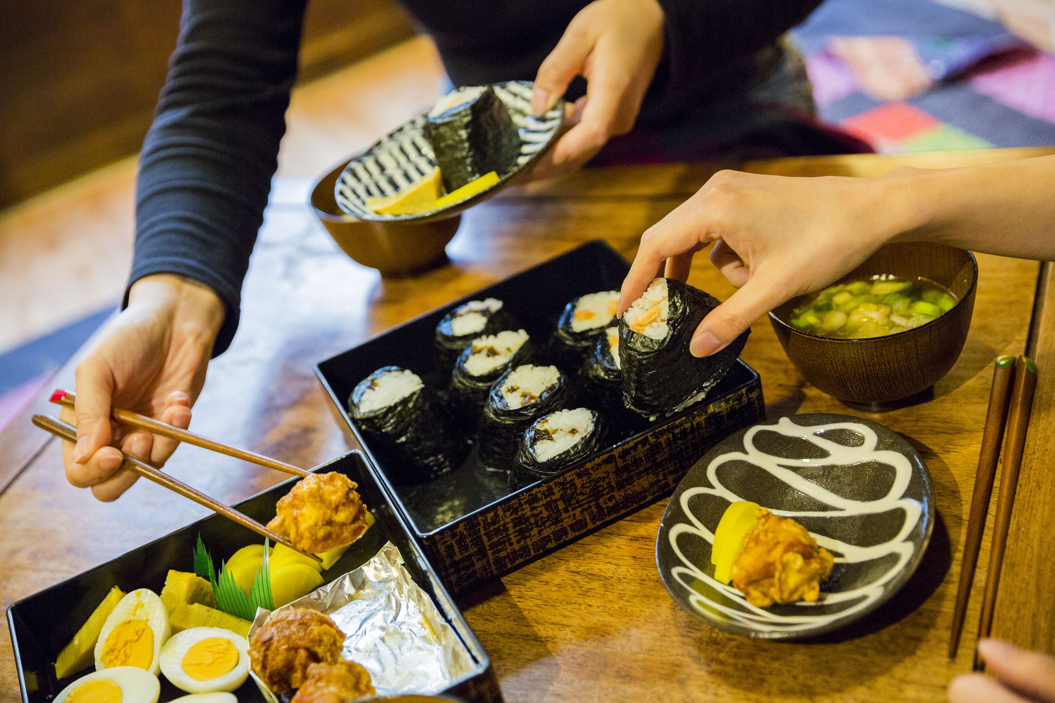 Ein Esstisch mit Sushi, einer Suppenschüssel und einem Teller mit gekochtem Ei und gebratenem Hähnchen.
