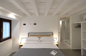 A bedroom with a bed, bedside tables, a wardrobe, and a shower area. - Piano Tre (Verona)